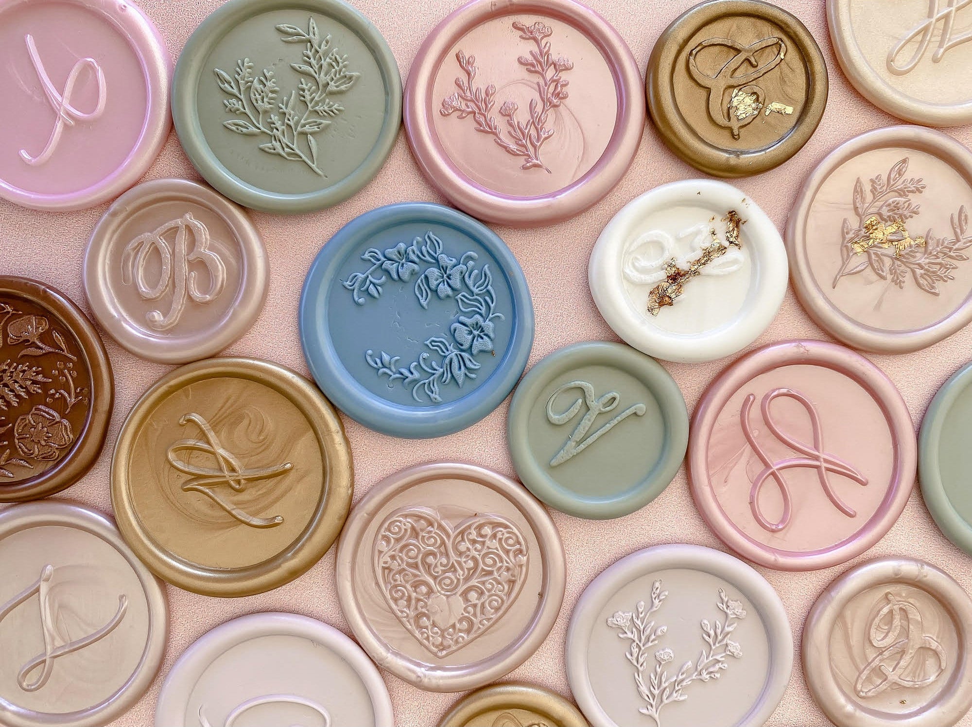Collection of decorative wax seals with various designs and lettering on a pink background.